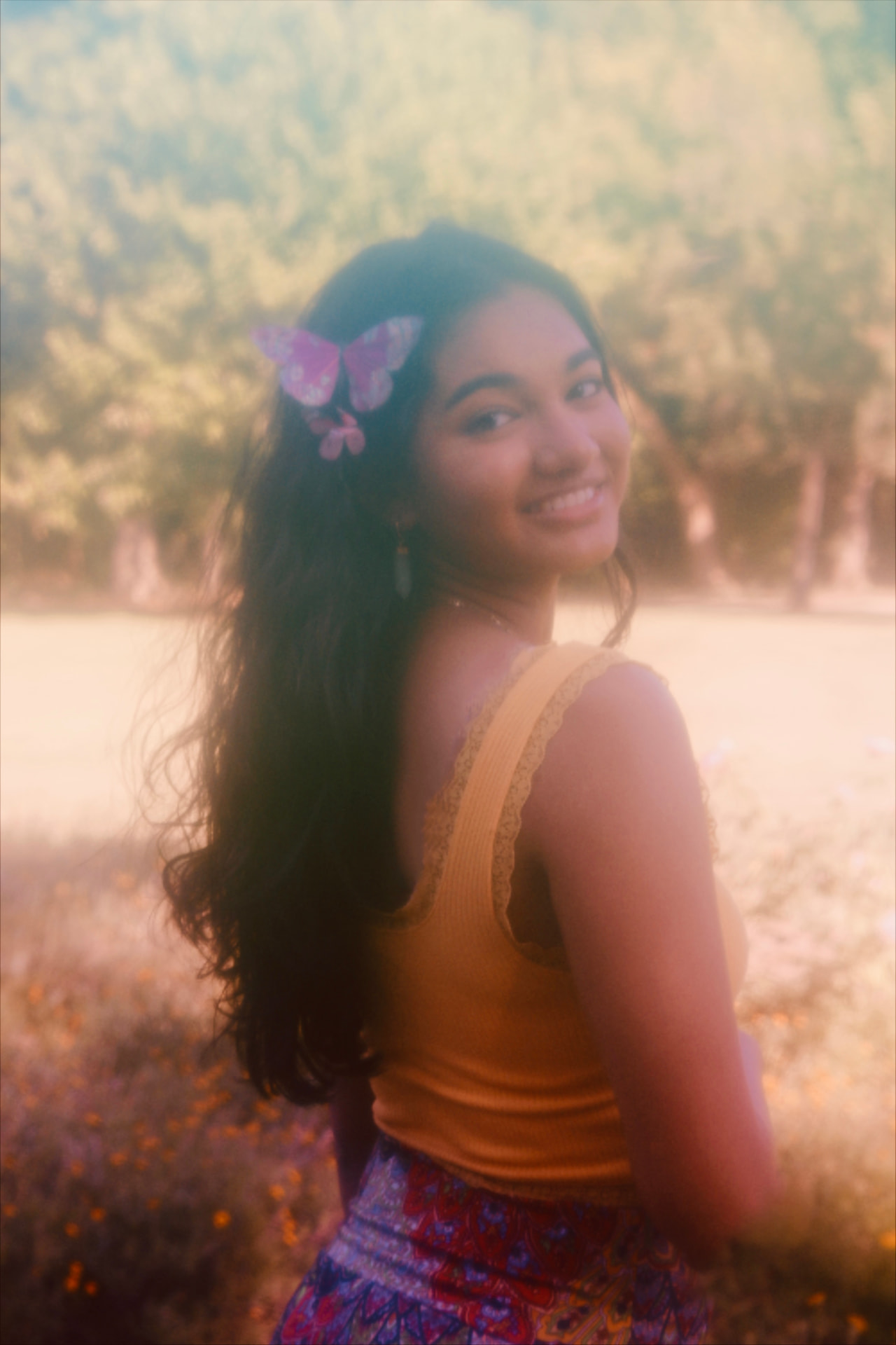 A woman glancing back over her shoulder in a golden field, pink butterfly pinned in her hair