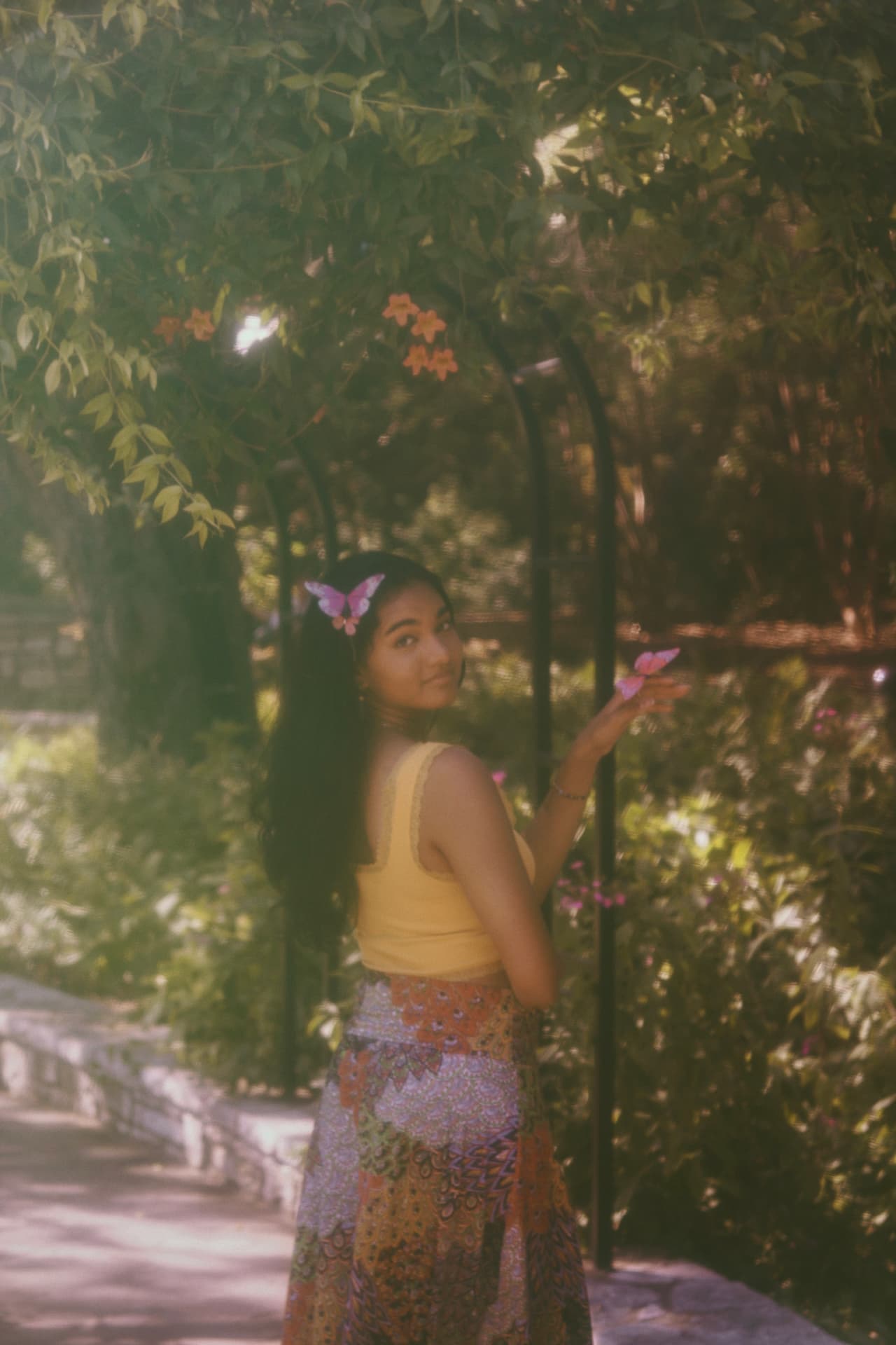 A woman beneath a rose-covered garden arch, pink butterflies pinned in her hair