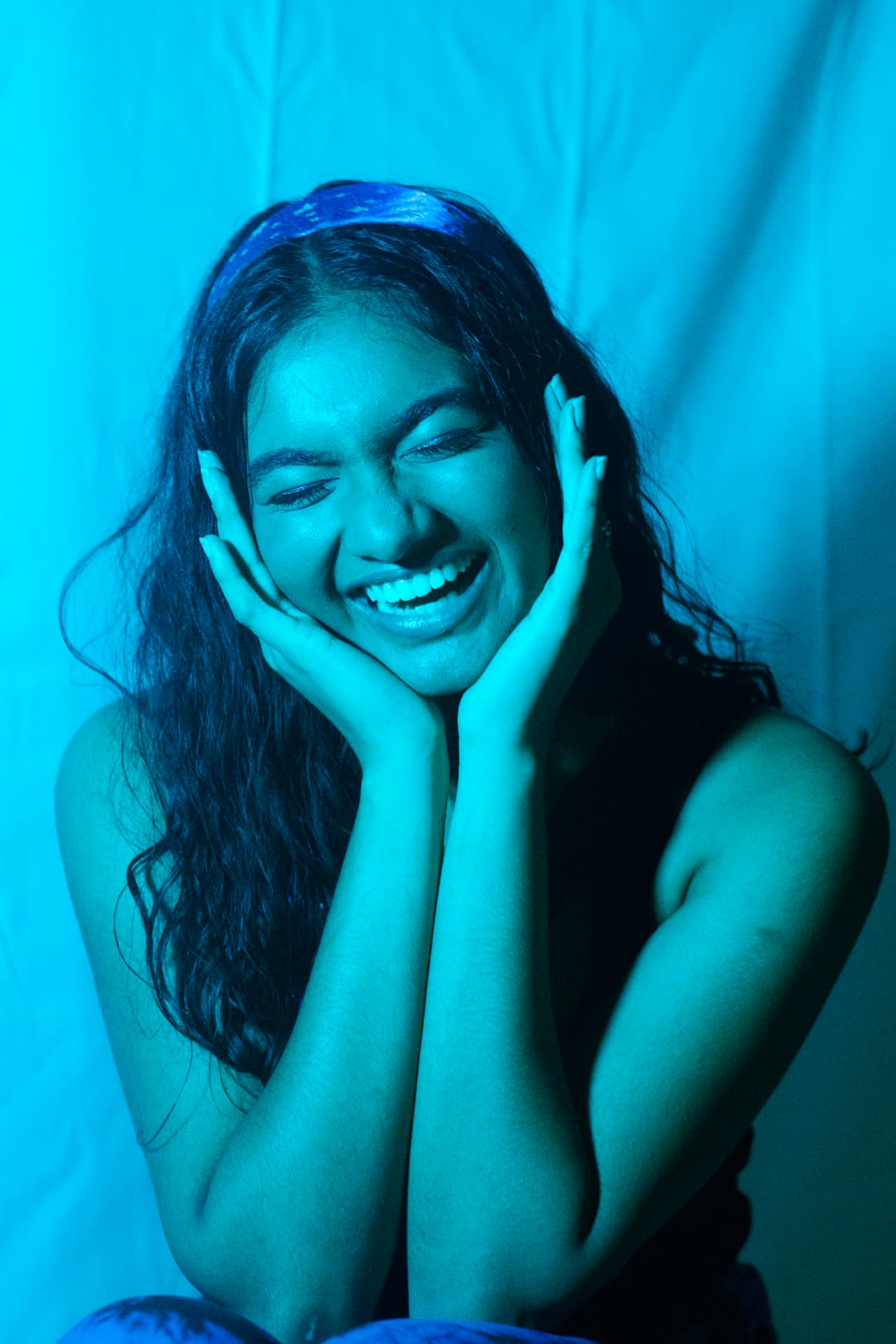 Joyful portrait of a woman with her face in her hands, lit entirely in cyan blue