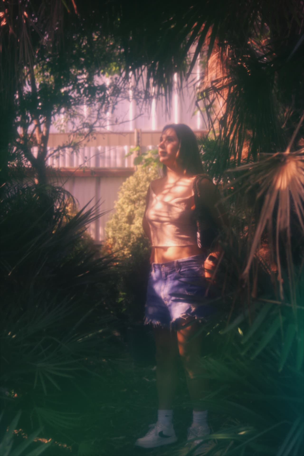 A woman framed by tropical leaves, dappled light across her face