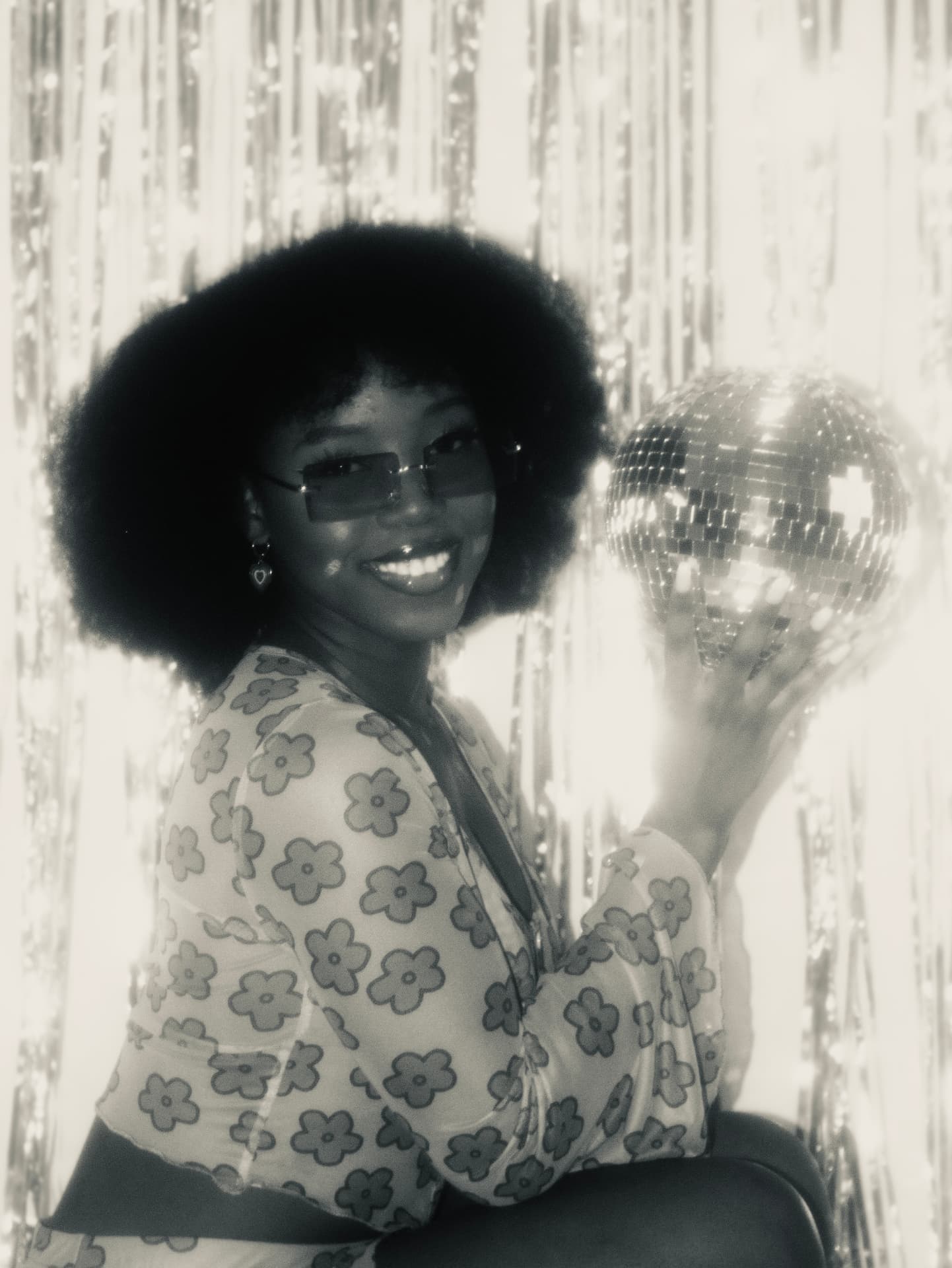 Smiling woman holding a mirrorball before a tinsel curtain