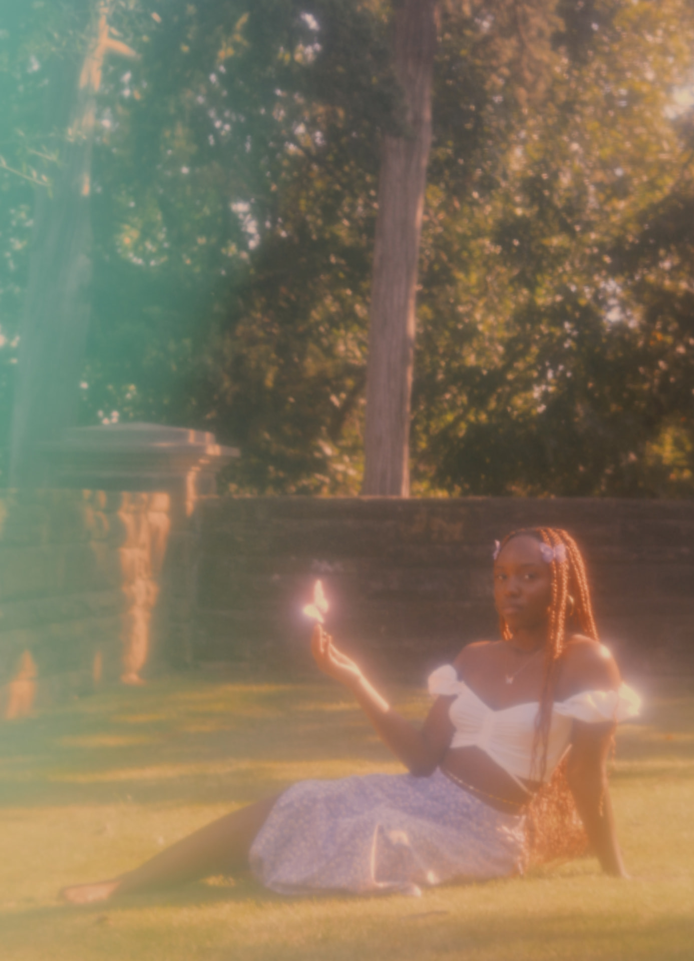 A woman seated on a sunlit lawn holding a glowing butterfly, long shot through heavy golden haze