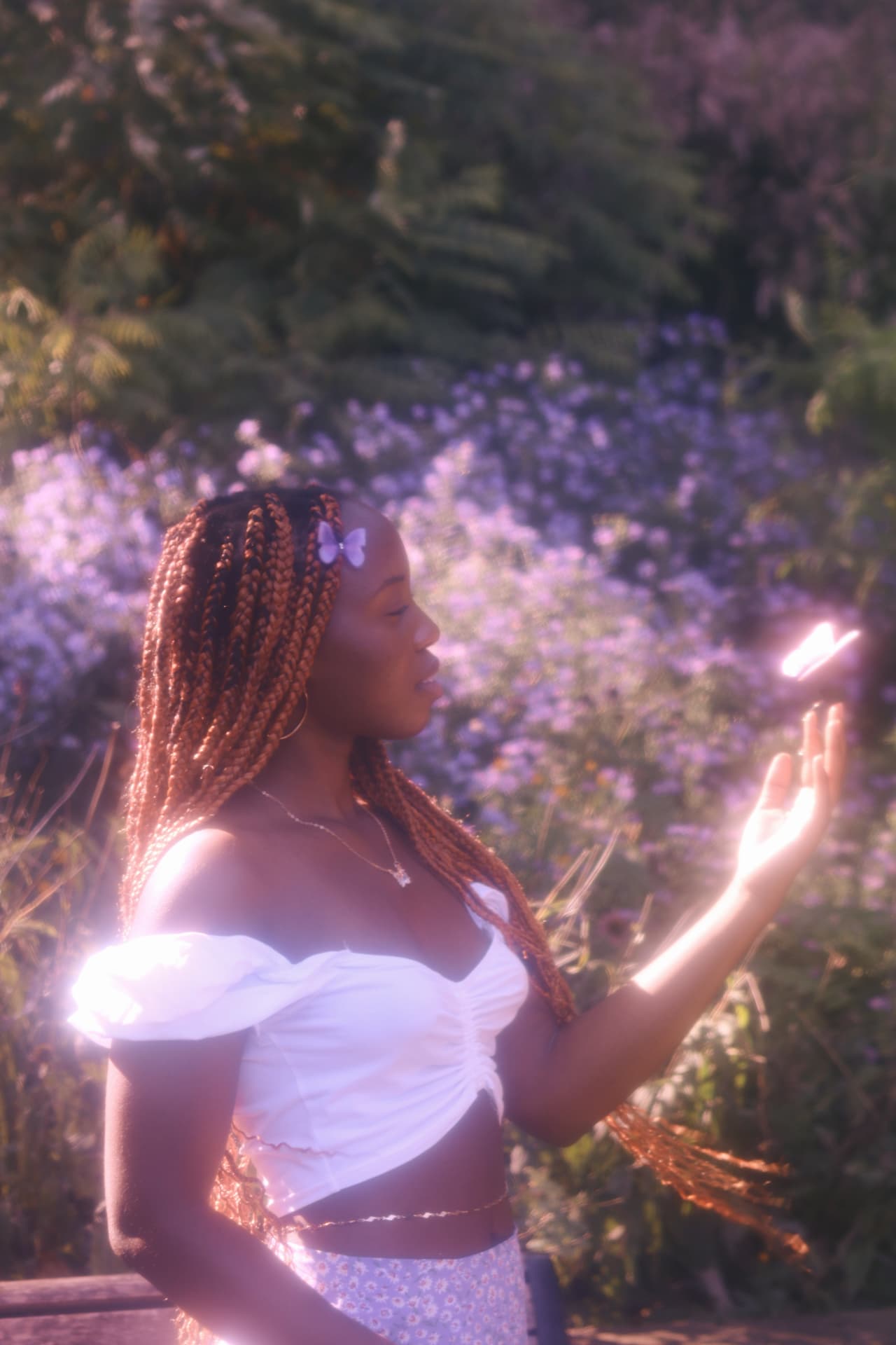 A woman with long braids bathed in warm haze, a glowing butterfly hovering above her open hand