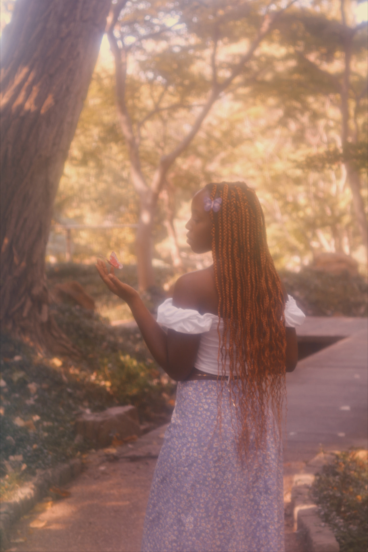 Woman beneath sunlit trees with a butterfly resting on her hand