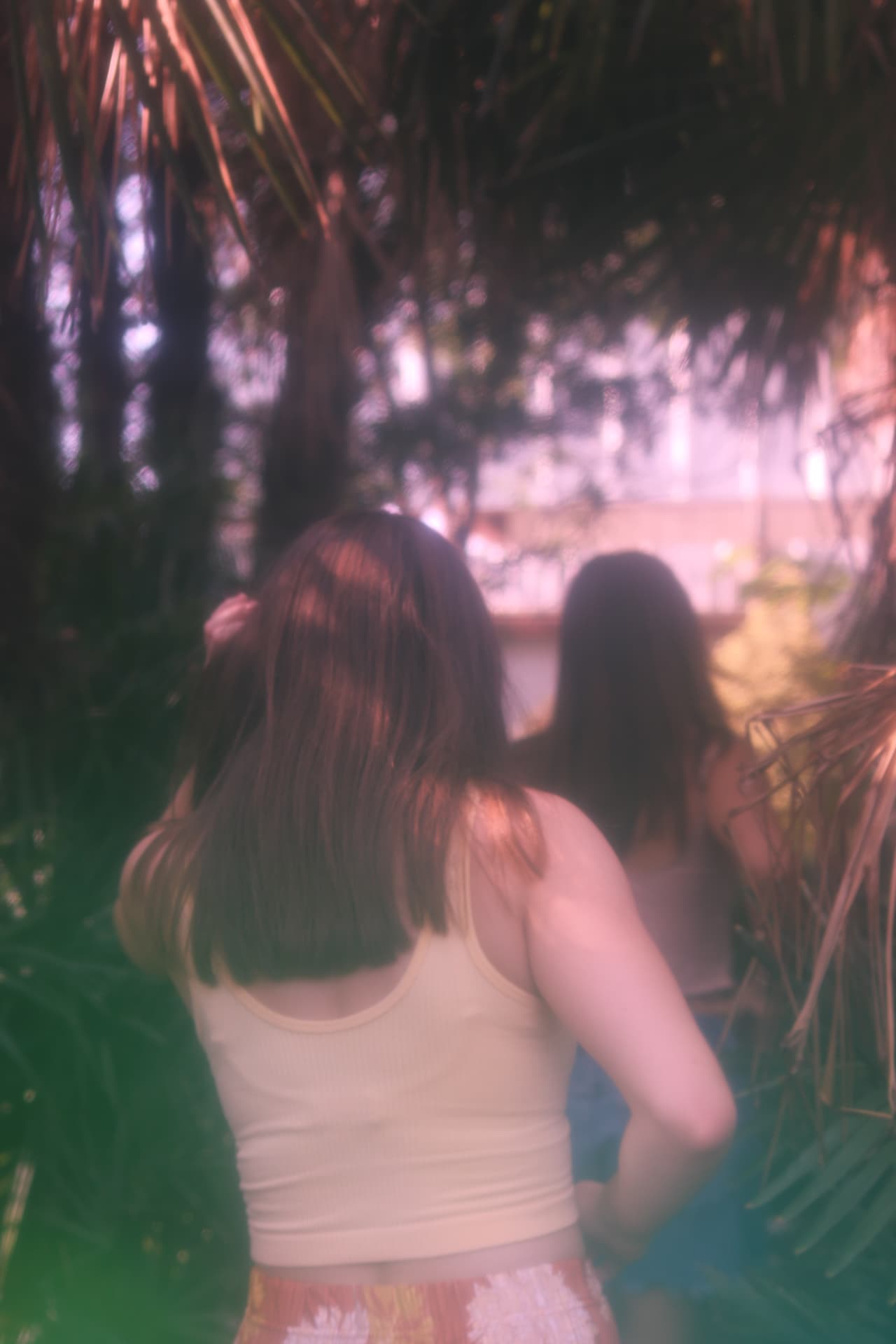 Two women dissolving into pink and green light beneath palm fronds
