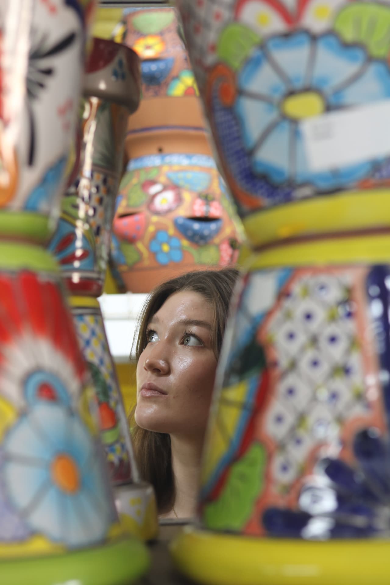 A woman gazing upward through a dense market of hand-painted talavera pottery