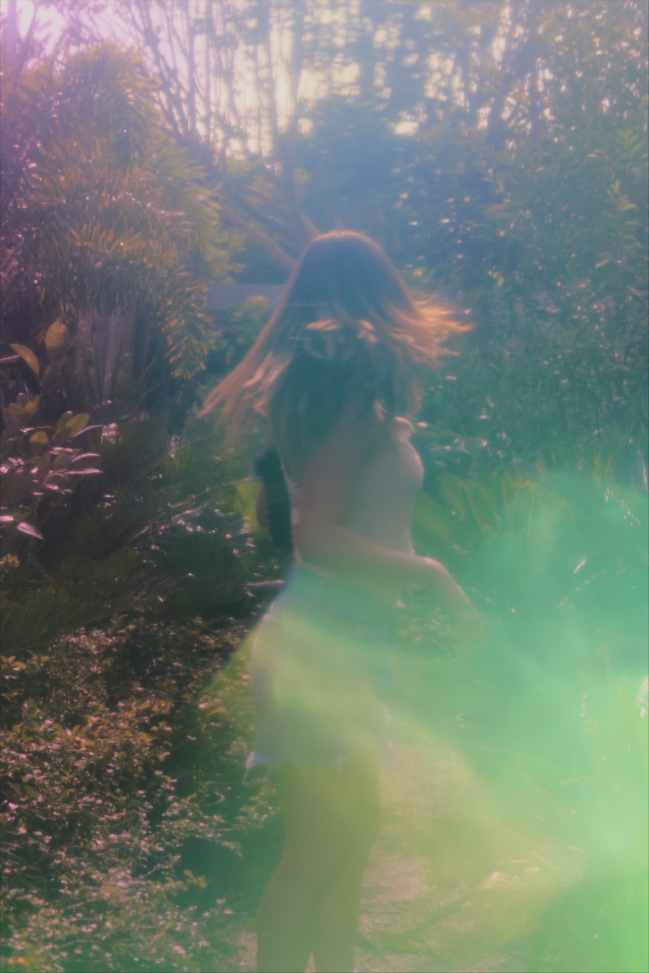 A woman walking through a sunlit garden refracted through a green and pink lens flare