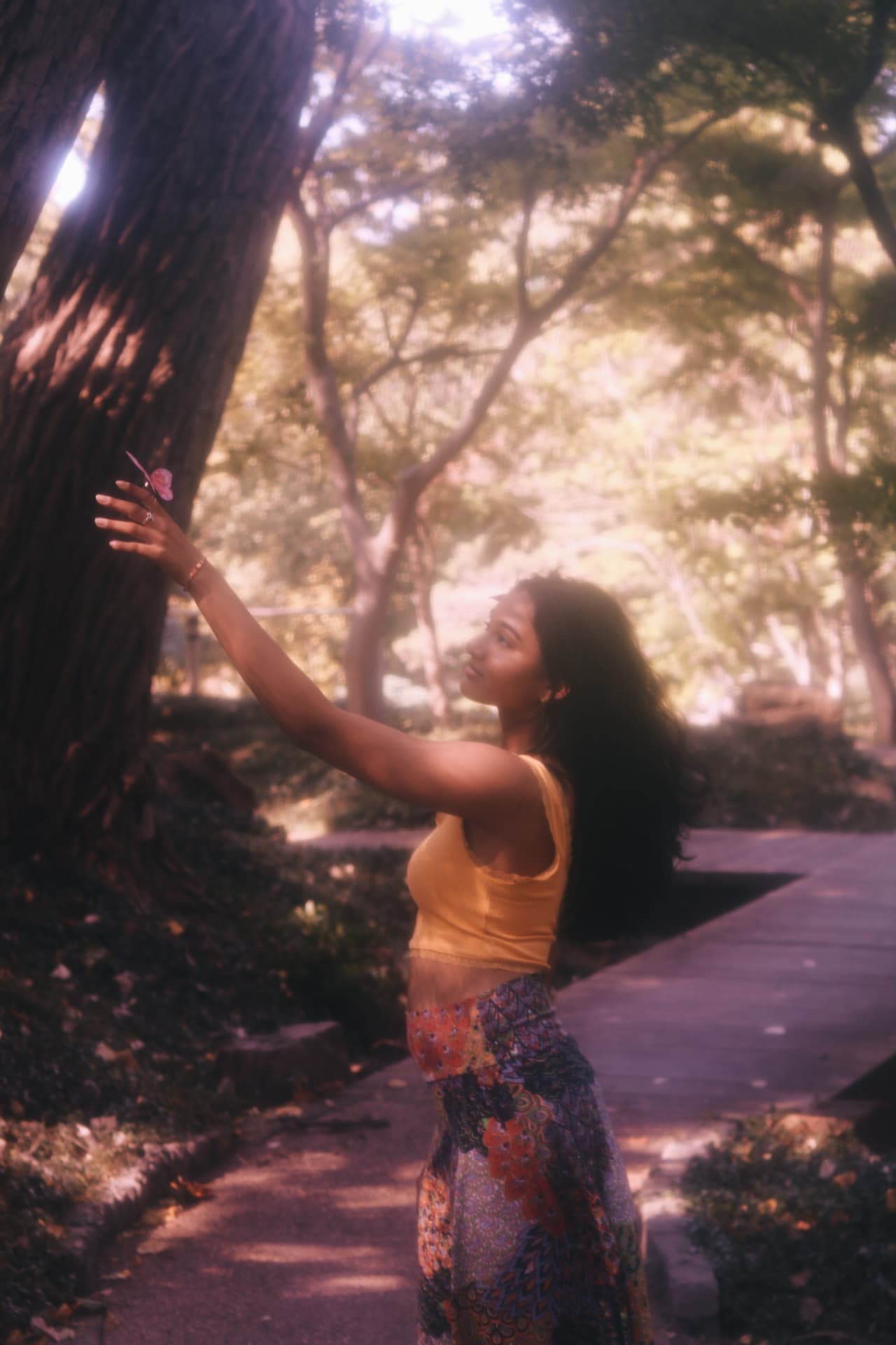A woman in a yellow top reaching toward a pink butterfly on a tree trunk, bathed in violet haze