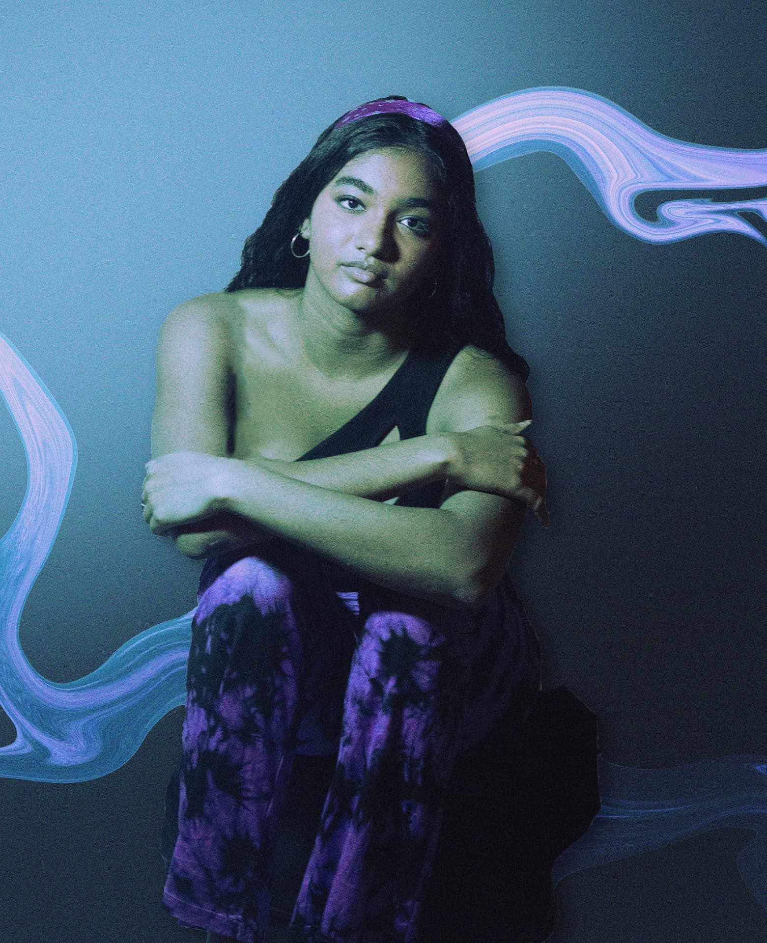 A seated figure in purple tie-dye against a dark studio backdrop, ringed by liquid light swirls